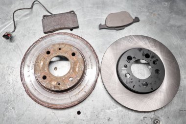 Old rusty brake disc and new disc. Change the old to new brake disc on car in a garage. Auto repair concept