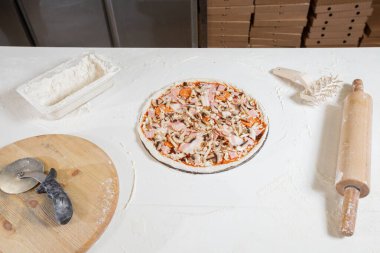 Closeup hand of chef baker in uniform blue apron cutting pizza at kitchen. High quality photo