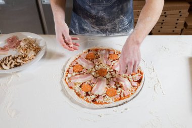Closeup hand of chef baker in uniform blue apron cutting pizza at kitchen. High quality photo