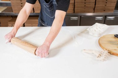 Closeup hand of chef baker in uniform blue apron cutting pizza at kitchen. High quality photo
