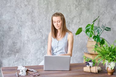 Genç bir bayan dizüstü bilgisayarda çalışıyor, sosyal ağlardaki mesajlara cevap veriyor. Çiçek teslimatı konsepti. Çiçekçide profesyonel işçi.