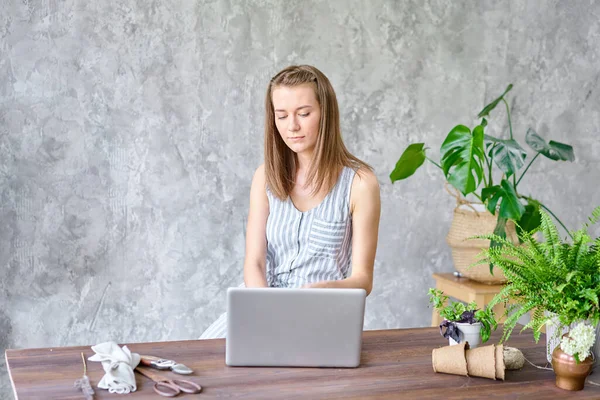 stock image Young female works on a laptop, responds to messages in social networks. Flower delivery concept. Professional worker in a flower shop