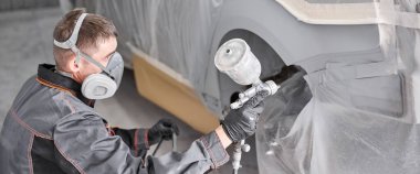 Arabanın arka tarafını boyayarak. Kostüm ve koruyucu giysiler giyen bir araba boyacısı. Araba servis istasyonu. Kazadan sonra araba tamiri..