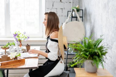 Genç bayan serbest çalışan dizüstü bilgisayarda çalışıyor, sosyal ağlardaki mesajlara cevap veriyor. Çiçek teslimatı konsepti. Çiçekçide profesyonel işçi.