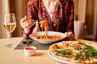 Woman eats Italian pasta with tomato, meat. Close-up spaghetti Bolognese wind it around a fork with a spoon. Parmesan cheese. clipart