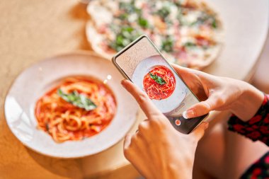 Cep telefonu olan bir kadın, yemek blogu ve sosyal ağlar için fotoğraf çekiyor. Domatesli İtalyan makarnası, et. Yakın plan spagetti Bolonez kaşıkla bir çatalın etrafına sarar..