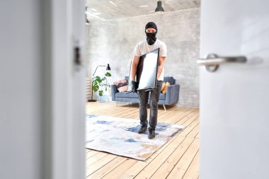 Modern pahalı televizyonu çalan siyah kar maskeli bir hırsız. Maskeli yüz. Hırsız evden televizyon çalıyor..