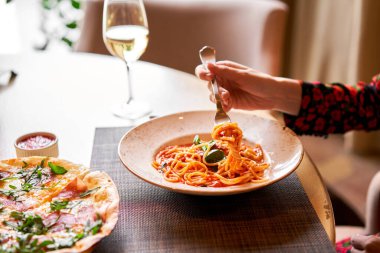 Kadın domatesli İtalyan makarnası yiyor, et yiyor. Yakın plan spagetti bolonezi kaşıkla bir çatalın etrafına sarıyor. Parmesan peyniri.