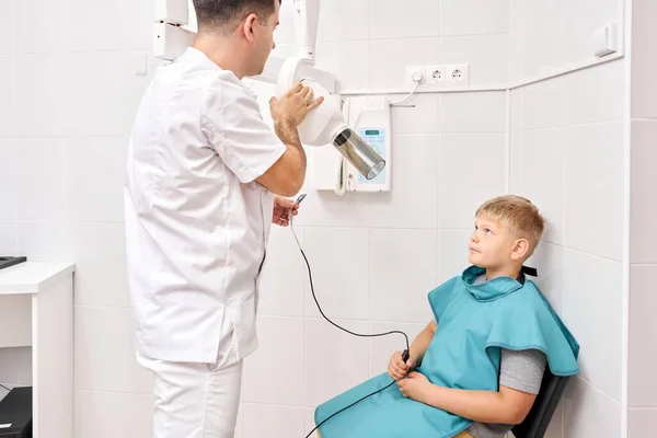 Radiographer taking teeth radiography to a boy using digital x-ray machine in pediatric dental clinic. Dentist prepares boy for tooth x-ray image in dental clinic