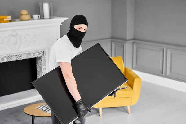 用黑色巴拉克拉瓦偷窃现代昂贵电视机的贼 蒙面脸男子窃贼从家里偷电视机 — 图库照片
