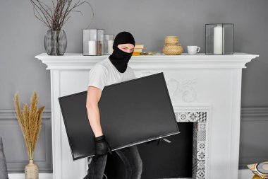 Modern pahalı televizyonu çalan siyah kar maskeli bir hırsız. Maskeli yüz. Hırsız evden televizyon çalıyor..