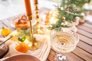 Noel yemeği ziyafeti. Küçük bir masa aperatifler, bruschetalar ve kanepelerle servis edilir. Şampanya bardakları, mumlar ve Noel ağacıyla süslü bir yemek masası. Arka planda bir çelenk..