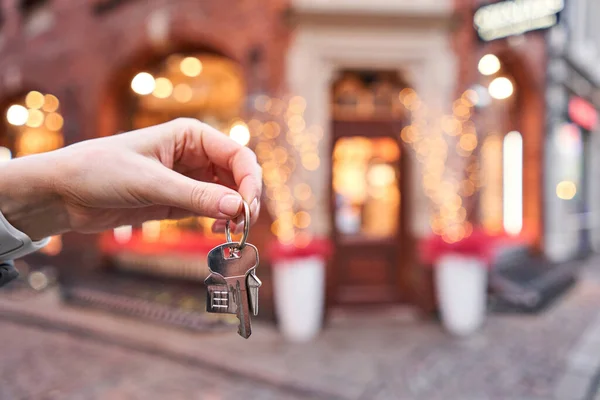 Stock image Mortgage or rent concept. Woman holding key with wooden house keychain . Real estate, hypothec, moving home or renting property. Christmas mood in blurred background.