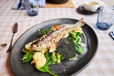 Roasted pike perch or cod fish with baked vegetables and spinach. Dish decorated with a slice of lemon. Restaurant menu.