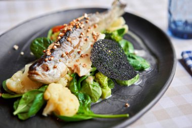 Roasted pike perch or cod fish with baked vegetables and spinach. Dish decorated with a slice of lemon. Restaurant menu.