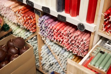 Many multicolored colorful paraffin stick Pastel colors candles arranged in shelves lying on shelter and sorted by color in a household candle shop store market