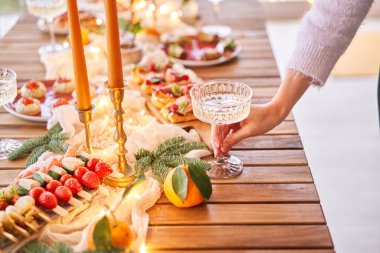 Noel yemeği ziyafeti. Küçük bir masa aperatifler, bruschetalar ve kanepelerle servis edilir. Şampanya bardakları, mumlar ve Noel ağacıyla süslü bir yemek masası. Arka planda bir çelenk..