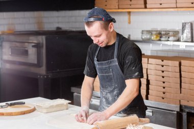 Closeup hand of chef baker in uniform blue apron cutting pizza at kitchen. High quality photo