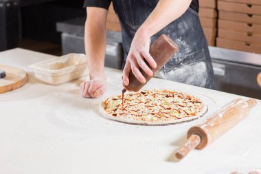 Closeup hand of chef baker in uniform blue apron cutting pizza at kitchen. High quality photo
