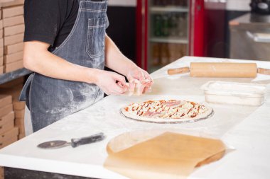 Closeup hand of chef baker in uniform blue apron cutting pizza at kitchen. High quality photo