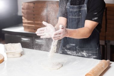 Closeup hand of chef baker in uniform blue apron cutting pizza at kitchen. High quality photo