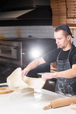 Closeup hand of chef baker in uniform blue apron cutting pizza at kitchen. High quality photo