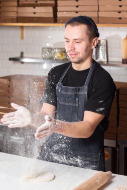 Closeup hand of chef baker in uniform blue apron cutting pizza at kitchen. High quality photo