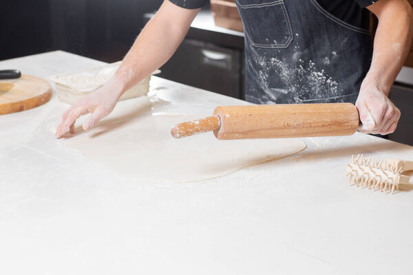 Closeup hand of chef baker in uniform blue apron cutting pizza at kitchen. High quality photo