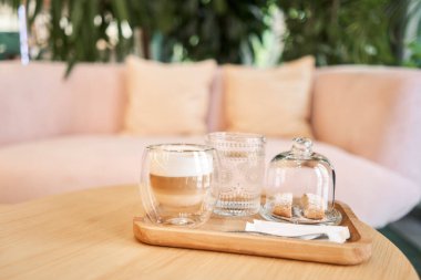 Bir fincan cantuccini ve ahşap tepside bir bardak su. Sütlü kahve, kurabiye ve cam sehpanın üzerinde su olan bir bardak. Yüksek kalite fotoğraf