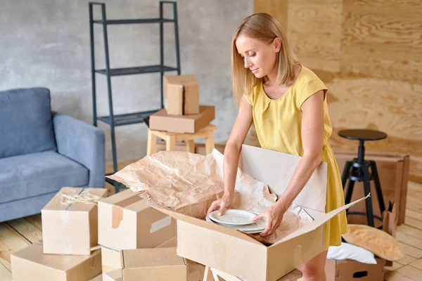 Young girl packing plates into the boxes ready to move. Woman unpacking moving boxes in her new home. unpack personal stuff from carton boxes. High quality photo