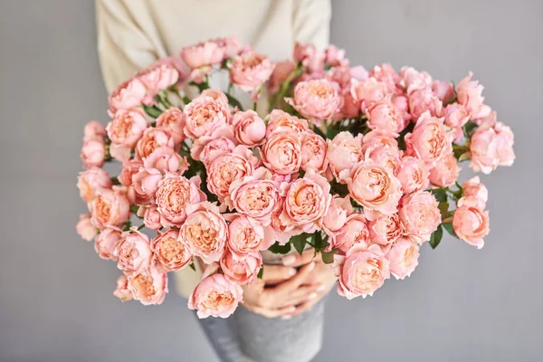A woman holds an aluminum vase with peach-colored bush spray roses in her hands. The florist takes care of the flowers. A girl with a vase of flowers in her hands. High quality photo
