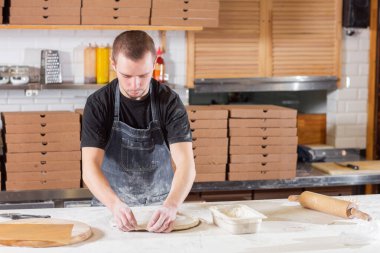 Closeup hand of chef baker in uniform blue apron cutting pizza at kitchen. High quality photo