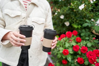 Mahalledeki bir kız elinde kahve bardakları tutuyor. Genç bir kadının elinde iki bardak sıcak içecek. Kahvaltı hazırda bekliyor. Piknik ve dışarı çıkma konsepti. - Evet. Yüksek kalite fotoğraf