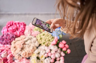 Genç bayan çiçekçi buketin fotoğrafını çeker. Kadın blogcu ve içerik yaratıcıları sosyal ağlar ve blog çiçekçisi. İnternet mağazası ve çiçek teslimatı konsepti. SMM terfisi. Yüksek kalite