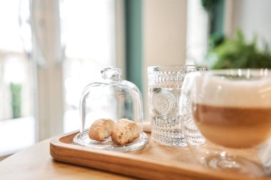 Bir fincan cantuccini ve ahşap tepside bir bardak su. Sütlü kahve, kurabiye ve cam sehpanın üzerinde su olan bir bardak. Yüksek kalite fotoğraf