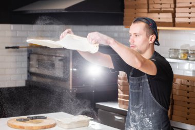 Closeup hand of chef baker in uniform blue apron cutting pizza at kitchen. High quality photo