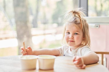 Tatlı küçük kız dondurma tatmaya hazırlanıyor. Güzel, büyüleyici bir bebek, pencerenin yanındaki kafede oturan bir masaya bakar. Çocuk Kafe 'si. Dondurma kafe 'nin içi. Yüksek