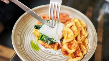 Hareketi Durdur. Kız haşlanmış yumurta keser ve yumurta sarısı akar. Patates waffle 'ı, somon ve yumurtalı avokado kreması. Sağlıklı kahvaltı, protein. Restoran yemeği. Hareketi Durdur