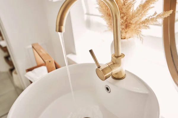 一个漂亮的水池 有一个金色水龙头 旁边是一个椭圆形的镜子和一个架子与手巾 在浴室水池里的精致的金色水龙头的特写 旁边是时尚的装饰 高质量的照片 — 图库照片
