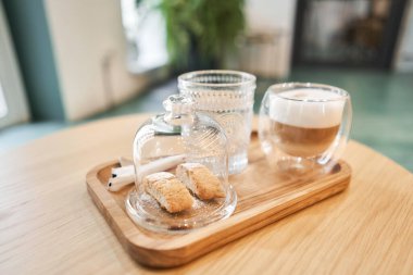 Bir fincan cantuccini ve ahşap tepside bir bardak su. Sütlü kahve, kurabiye ve cam sehpanın üzerinde su olan bir bardak. Yüksek kalite fotoğraf