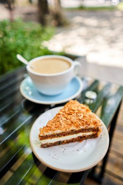Bir fincan sıcak Peanut latte ve havuçlu kek. Kahve dükkanının ortak çalışma alanındaki masa. Güneşli bir günde verandada bir fincan kahve. Kafede kahve molası. Yakın plan. Yüksek kalite fotoğraf.