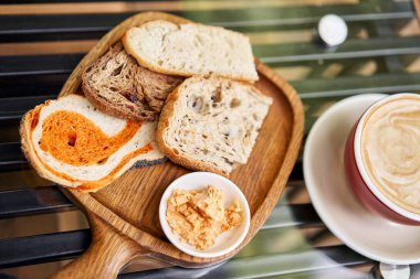Tahtada dilimlenmiş ekmek. Tütsülenmiş tereyağı ile servis edilir. Cappuccino kahveli kahvaltı. Ahşap tabakta tereyağı ve ekmek kompozisyonu. Yüksek kalite fotoğraf