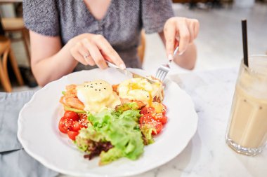 Kadın haşlanmış yumurta keser ve yumurta sarısı akar. Brioche, somon ve yumurtalı avokado kreması. Sağlıklı kahvaltı, protein. Restoran yemeği.