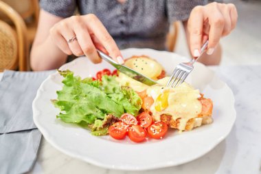 Kadın haşlanmış yumurta keser ve yumurta sarısı akar. Brioche, somon ve yumurtalı avokado kreması. Sağlıklı kahvaltı, protein. Restoran yemeği.