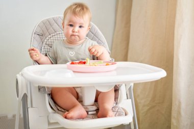 Tatlı çocuk sağlıklı makarna ve sebze buğulama yiyor. 10 aylık güzel bir kızın portreleri. Bebek bebekler için özel bir sandalyede oturuyor. Yüksek kalite fotoğraf