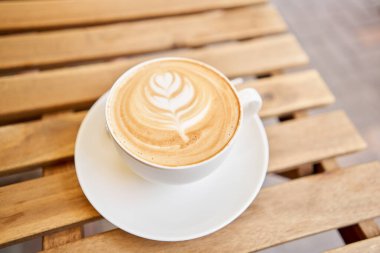 Bir fincan sıcak kapuçino. Kahve dükkanının ortak çalışma alanındaki masa. Güneşli bir günde verandada bir fincan kahve. Kafede kahve molası. Yakın plan. Yüksek kalite fotoğraf.