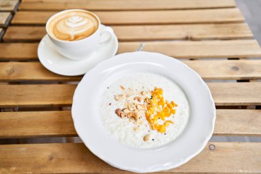 Güneşli bir sabahta, verandada, kafede kahvaltı. Cappuccino kahve ve mango, kaju fıstığı ve susam tohumlu pirinç lapası. Kahvaltıda. Yüksek kalite fotoğraf