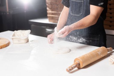 Closeup hand of chef baker in uniform blue apron cutting pizza at kitchen. High quality photo