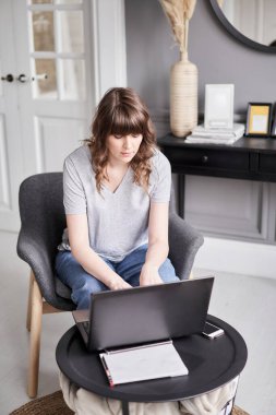 Evdeki oturma odasında kanepede otururken siyah dizüstü bilgisayar kullanan güzel, neşeli bir kız. Genç bir kadın iletişim ve iş için dizüstü bilgisayar kullanıyor. Evet.