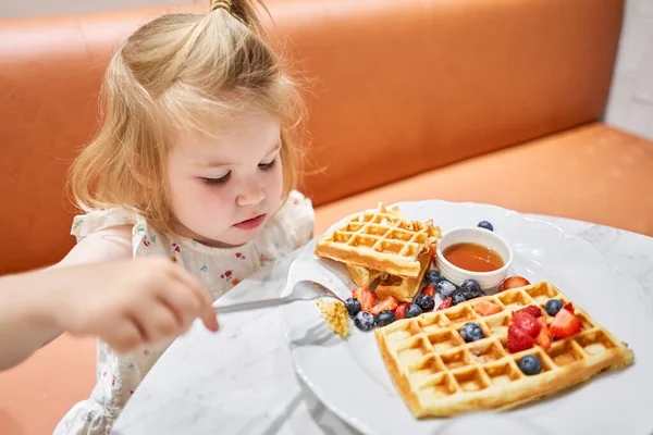 幸せな3歳の女の子を食べる カフェで朝食 アイスクリーム ベリー メープルシロップ付きのクラシックウィーンのワッフル レストランのテーブル 高品質の写真 — ストック写真